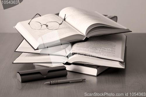 Image of opened books pen and glasses on sepia background