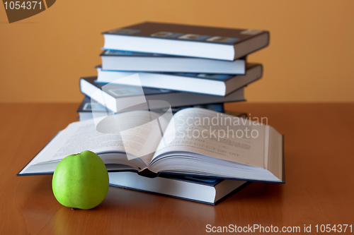 Image of green apple and opened books on the desk