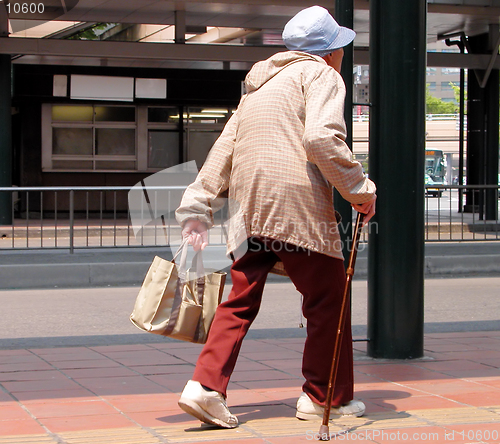 Image of    An old woman with bag walking in a bus station-Japan