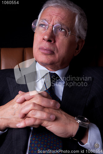 Image of Pensive mature businessman seated on a chair, looking up