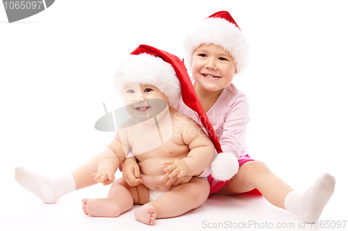 Image of Two children wearing red Christmas caps and smile