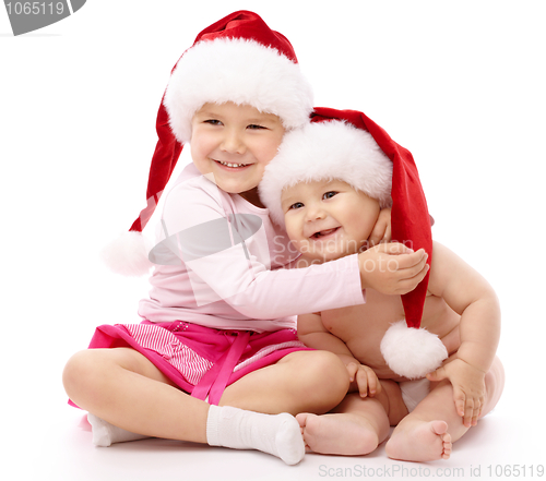 Image of Two children wearing red Christmas caps and smile