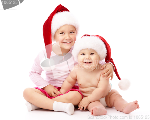 Image of Two children wearing red Christmas caps and smile