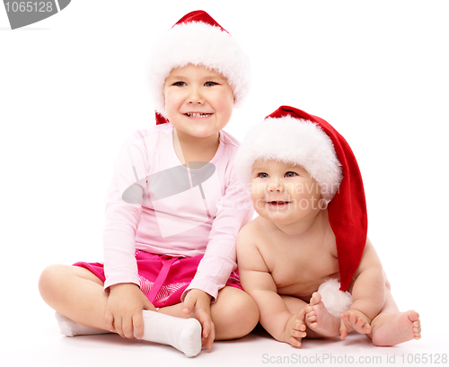 Image of Two children wearing red Christmas caps and smile