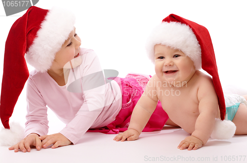 Image of Two children wearing red Christmas caps and smile