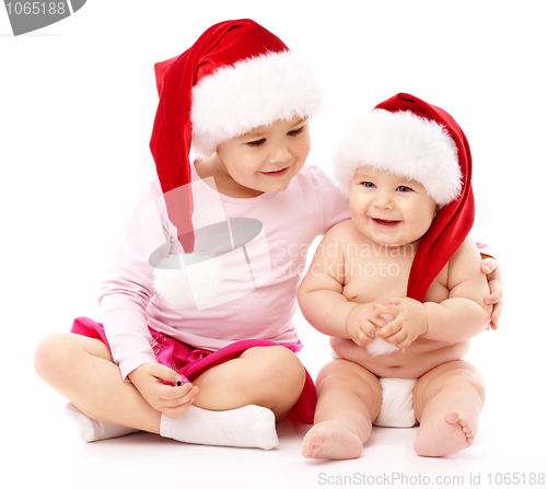 Image of Two children wearing red Christmas caps and smile