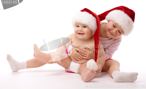 Image of Two children wearing red Christmas caps and smile