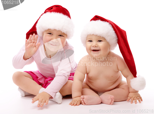 Image of Two children wearing red Christmas caps and smile