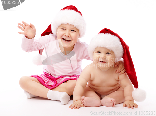 Image of Two children wearing red Christmas caps and smile