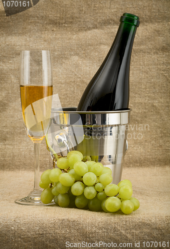 Image of Champagne bottle, bucket, goblet and grapes