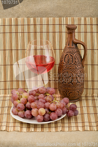 Image of Ceramic bottle, grape and goblet on mat