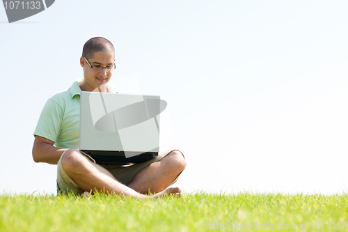 Image of A young men sit on the in the park using a laptop