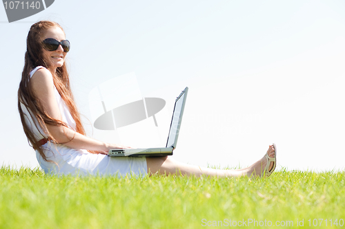 Image of young feamle sit in the park and using a laptop