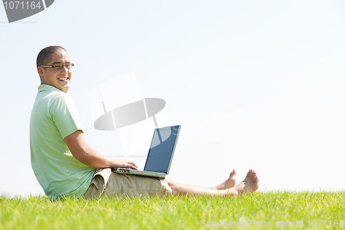 Image of A young men sit on the in the park using a laptop