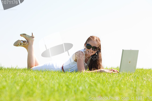 Image of oung female lying on the grass in the park using a laptop
