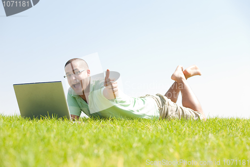 Image of A young men sit on the in the park using a laptop