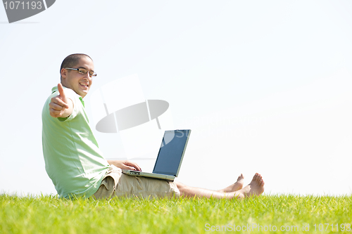 Image of A young men sit on the in the park using a laptop