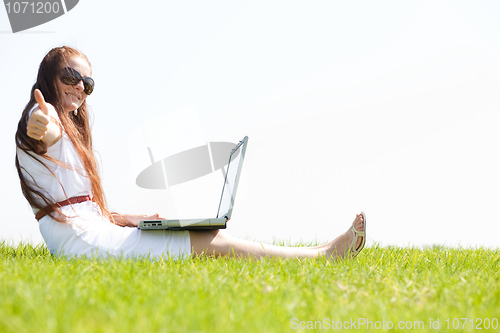 Image of young feamle sit in the park and using a laptop