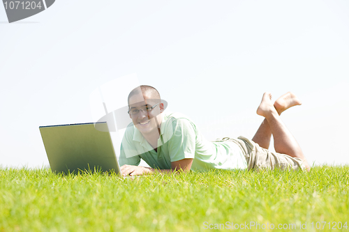 Image of A young men lying on the in the park using a laptop