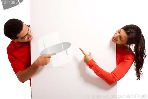 Image of Playful young couple pointing the blank white baord