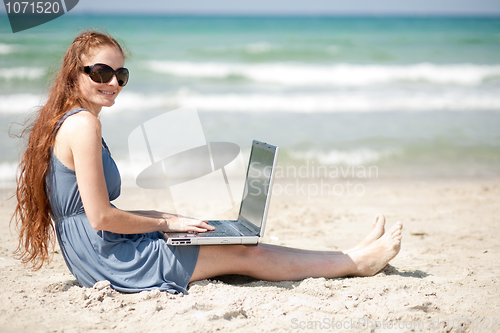 Image of Woman working on a laptop by sitting on the beach