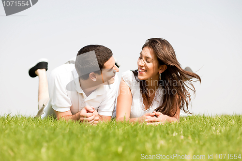 Image of young couple smiling by laying down in a green grass field