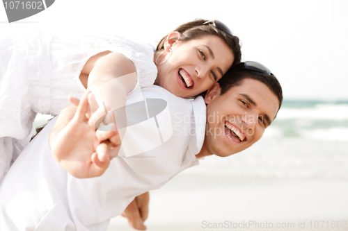 Image of Young man piggybacking his girlfriend at beach
