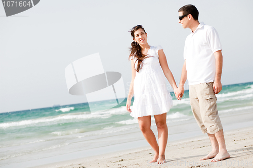 Image of Young couple holding hands and walking on the beach