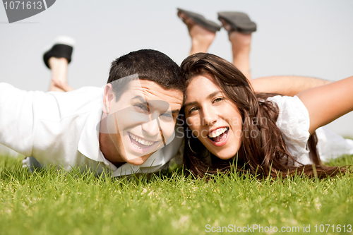 Image of Playful young couple laying down in a green grass field