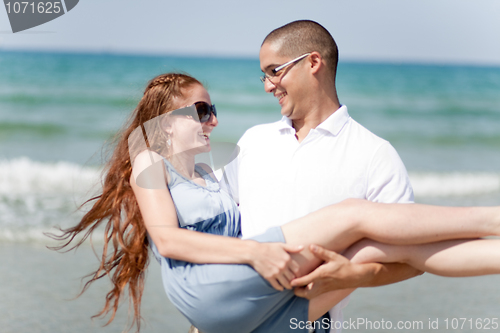 Image of Happy young man carriying his girl friend on the beach