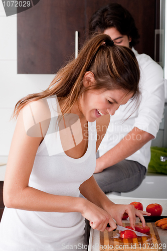 Image of playful young girlfriend using chopping board for slicing tomatoes