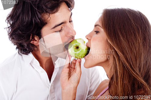 Image of young couple playfully biting green apple