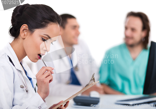 Image of Young asian doctor thinking with the pen, others blurred behind