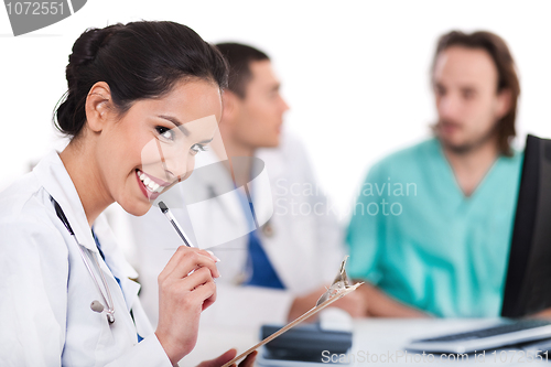 Image of Young asian doctor smiling with the pen and looking the camera, others blurred behind