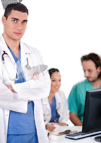 Image of Serious young doctor looking at the camera, two others making notes in the background