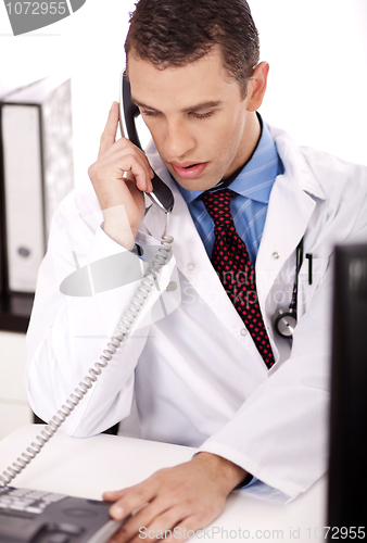Image of young physician sitting at his desk talking over phone