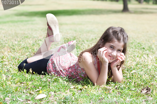 Image of happy cute girl  laying on a grass field and looking stright
