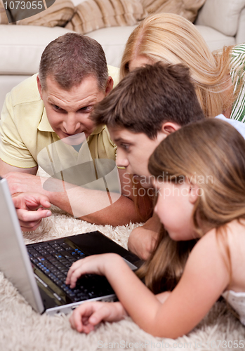 Image of Domestic family of four lying and working with laptop