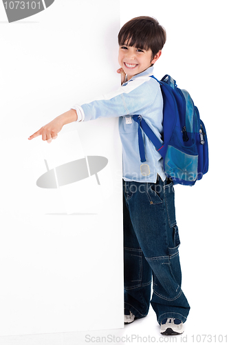 Image of Young kid happily standing behind the board and pointing to empty space