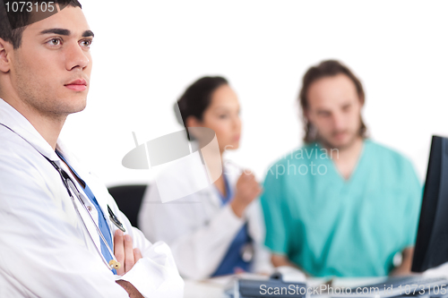 Image of Young doctor thinking deeply, collegues discussing behind with computer