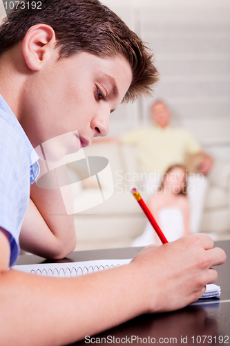 Image of Young teenager writing in his notebook in living room