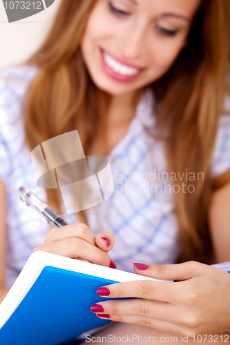 Image of Young woman sitting on sofa writing in notepad