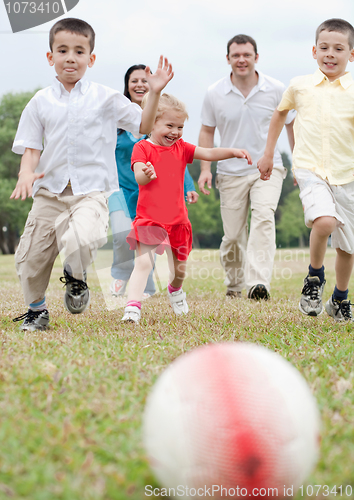 Image of Beautiful family of five on outdoors running towards the foot ball
