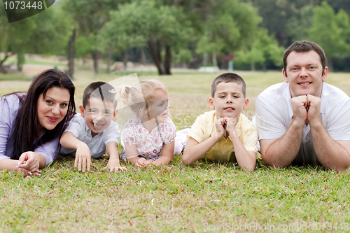 Image of Cheerful family of five lying on lawn in the green park