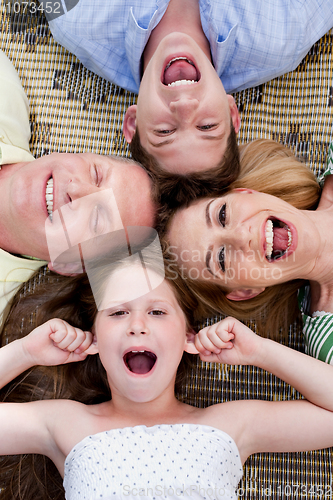 Image of Happy family of four lying on the carpet with their heads together