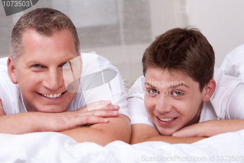 Image of Friendly father and son smiling and lying on the bed