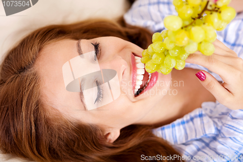 Image of Happy young woman eating grapes
