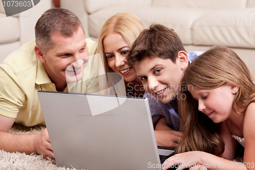 Image of Family lying on carpet in living room with laptop