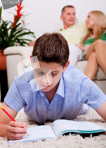 Image of Young boy studying with family in the background