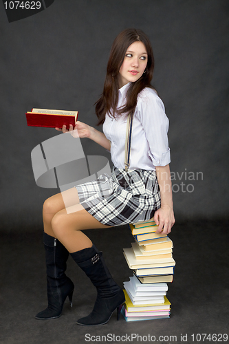 Image of Young woman sits on a pile of books